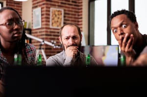 This is an image of three people looking at a laptop screen with shocked facial expressions