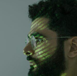 This is an image of a man's side profile with green code reflecting on his face.