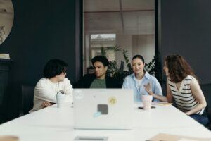 This is an image of four people sitting at a desk with an open laptop in front of them.