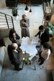 This image depicts three women, and two men gathered around a table looking at some corporate documents.