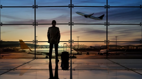 Business man standing in an airport looking out the window at a plane.