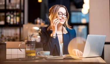 This is an image of a woman talking on the phone seated in front of an open laptop.