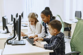 This is an image of children looking at a computer in school. 