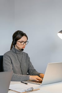This is an image of a woman working at a desk with a headset on.