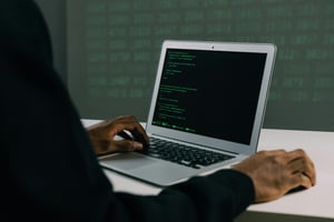 This is an image with a man sitting in front of a laptop with some code on it.