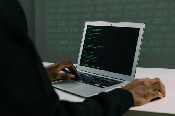 This is an image with a man sitting in front of a laptop with some code on it.