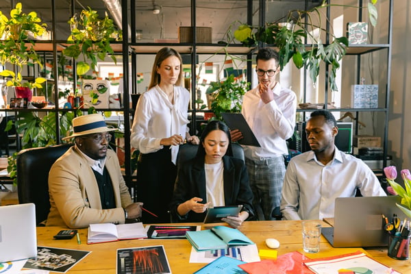 This is an image of people gathered at a board table and looking at a tablet. 
