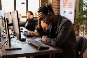This is an image of a frustrated call centre agent holding his head in his hand.