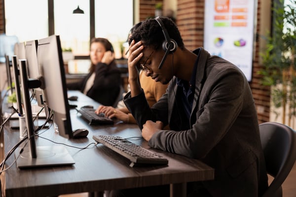 This is an image of a frustrated call centre agent holding his head in his hand.