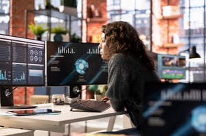 This is an image of a woman working at a desk with two monitors in front of her.