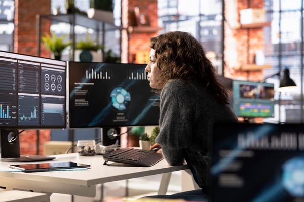 This is an image of a woman working at a desk with two monitors in front of her.