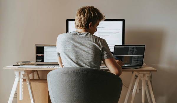 This is an image of a man working at a desk with three monitors in front of him.