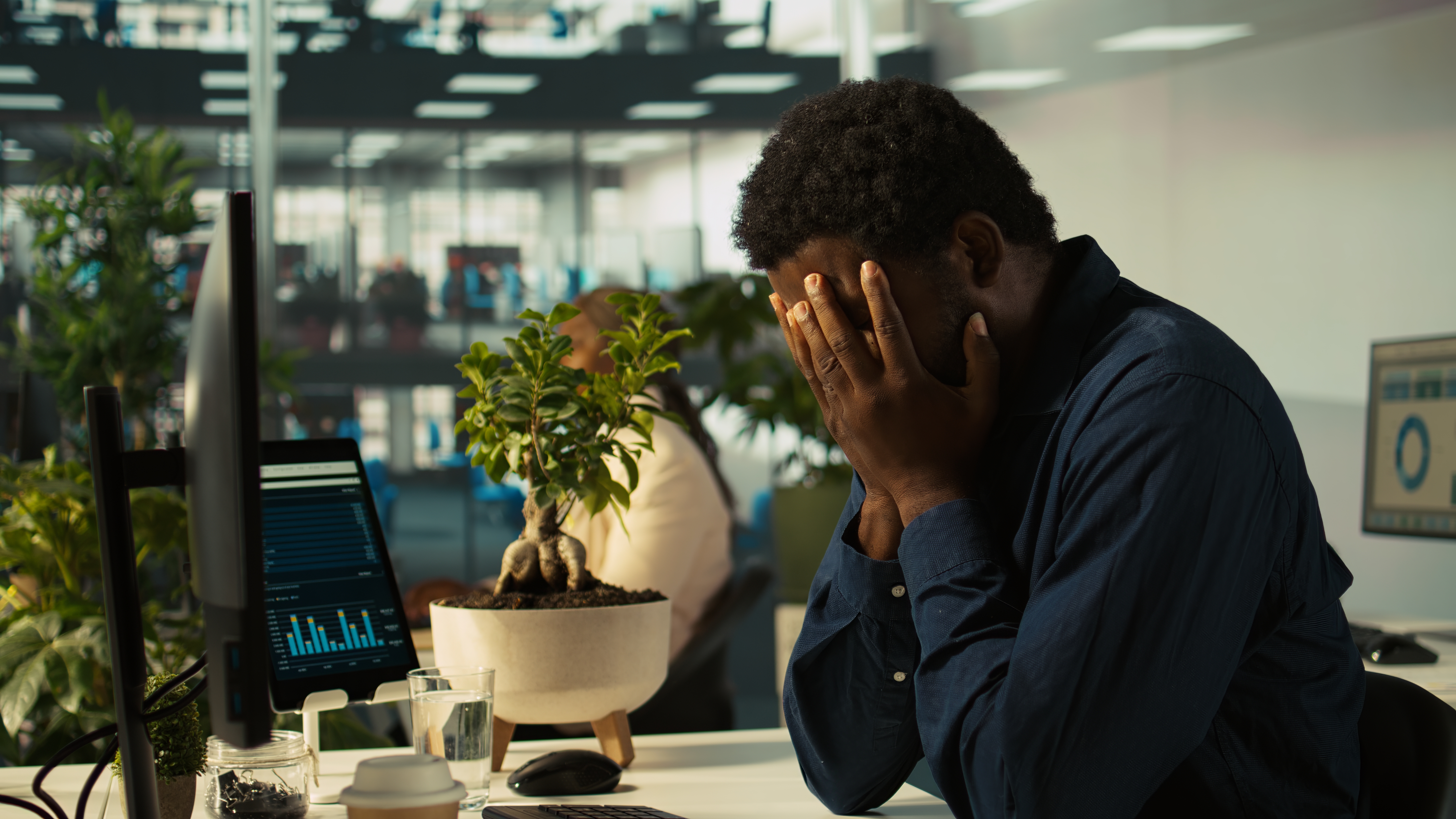 This is an image of a man sitting at a desk with his face in his hands